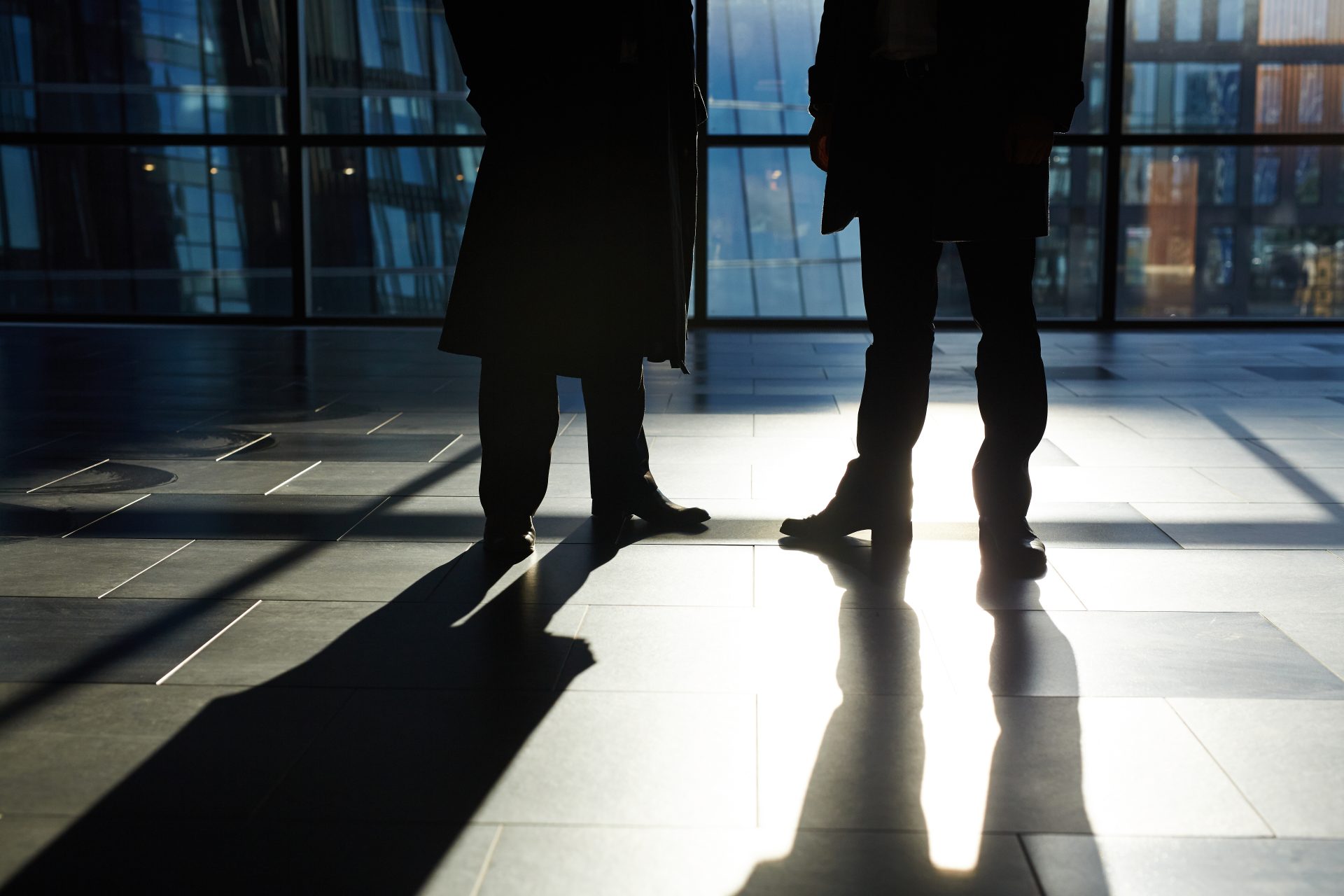 Storyblocks Two Unrecognizable White Collar Workers Standing Against Panoramic Window In Modern Office Lobby Their Shadows Reflecting On Tile Flooring S8zkMirwCb Scaled